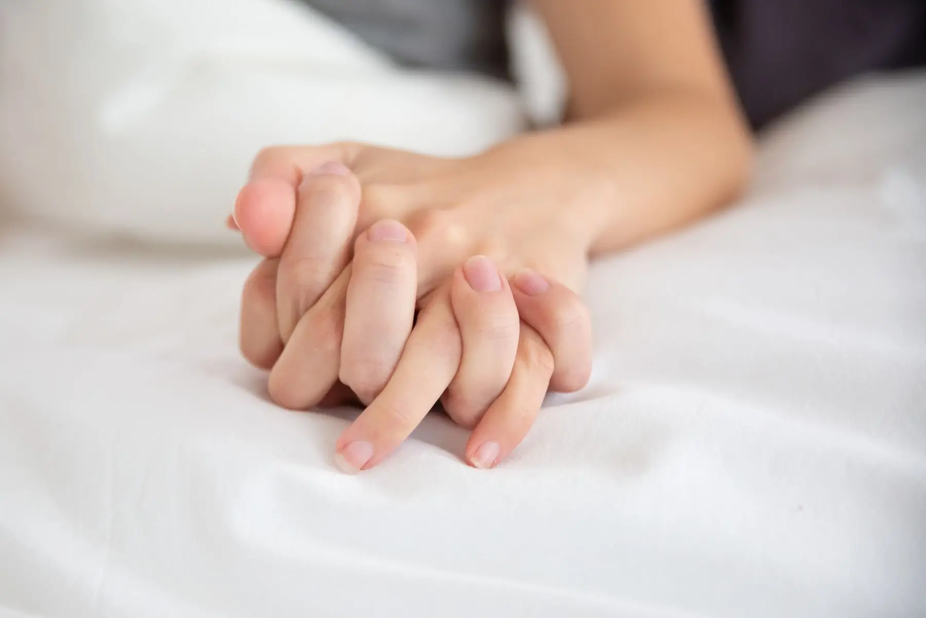 Ineinander verschränkte Hände eines Paares auf weißem Laken