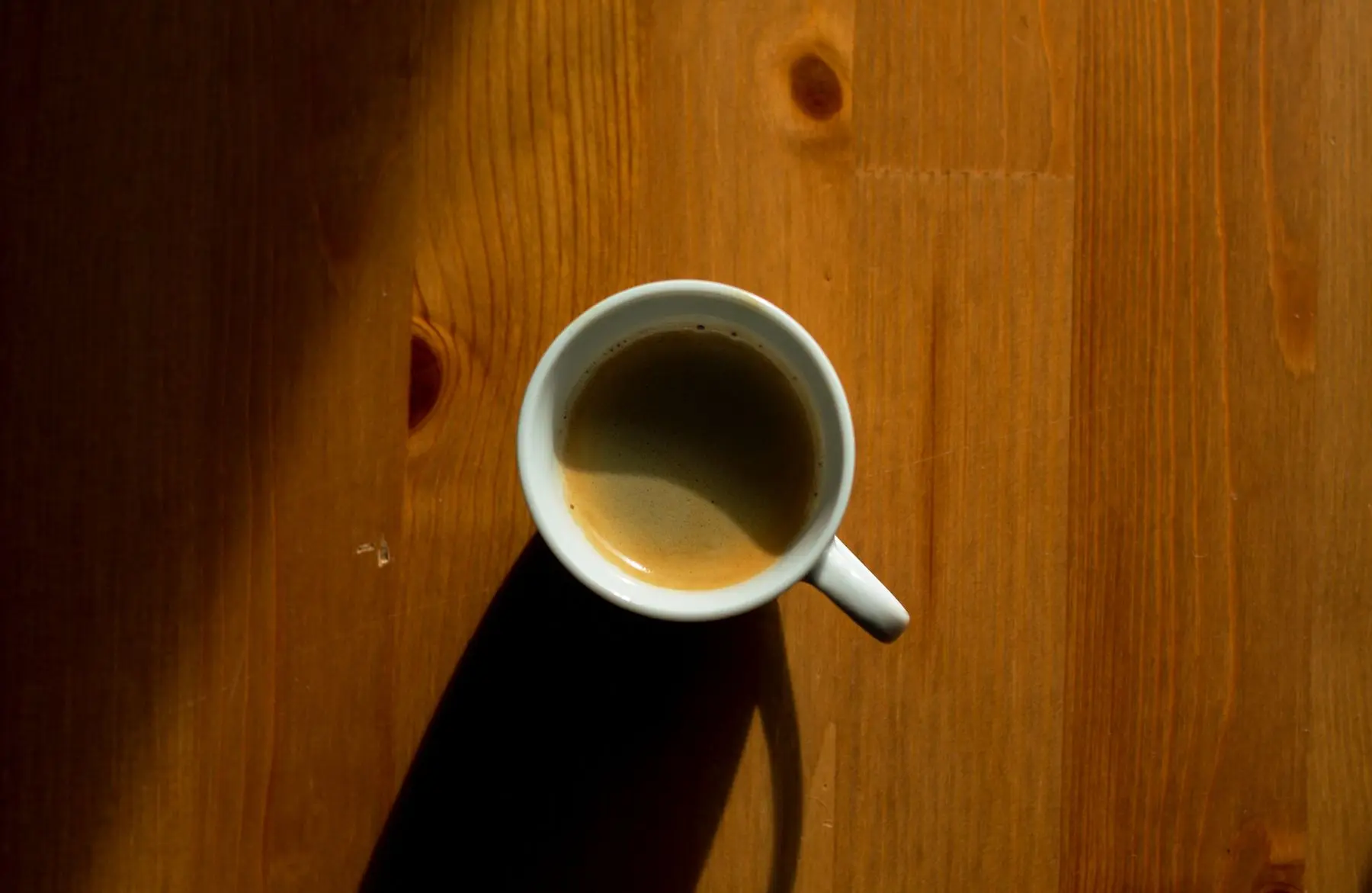 Kaffeetasse mit Schatten auf einem Holztisch